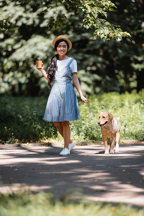 cheerful asian woman with takeaway drink walking with dog in park