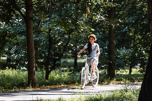 young asian woman in straw hat and sundress cycling in park