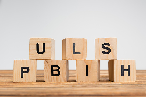 stack of cubes with black publish inscription on wooden surface isolated on grey