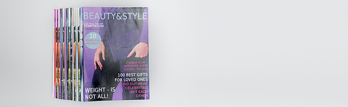 stack of beauty and style magazines isolated on grey, top view, banner