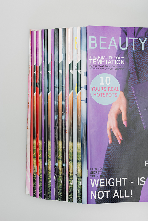 top view of beauty magazines stacked isolated on grey