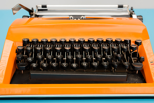 close up view of bright orange typewriter with black keyboard isolated on blue