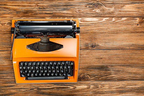 top view of orange typewriter on brown wooden surface