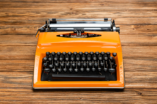 bright orange typewriter with black keyboard on textured wooden surface