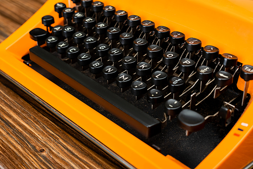 close up view of black keyboard of orange typewriter on wooden surface