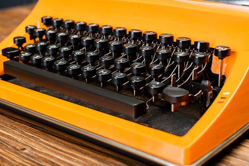 close up view of orange typewriter with black keyboard on wooden desk