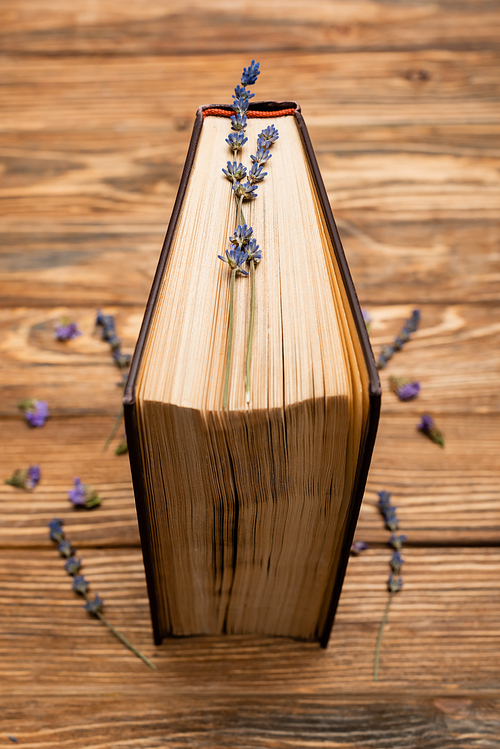 close up view of book with purple lavender flowers on blurred wooden surface