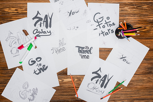 top view of white paper sheets with various fonts, color pencils and felt pens on wooden surface