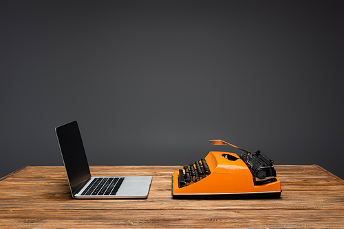 laptop with blank screen near typewriter on wooden desk isolated on grey