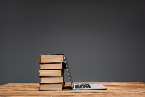 pile of books and laptop on brown wooden surface isolated on grey