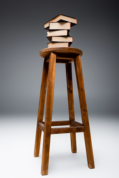 stack of books on wooden stool on grey background