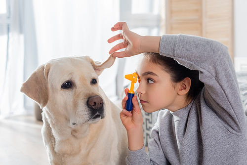 preteen girl examining ear of dog with otoscope while playing at home
