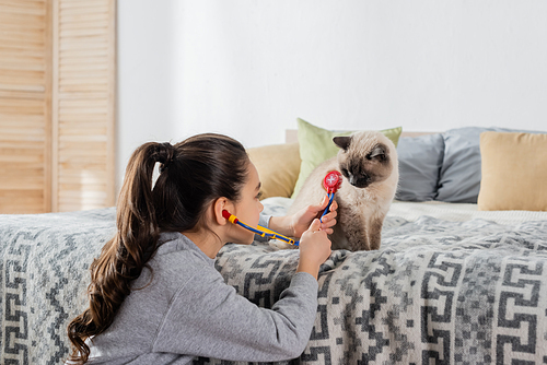 preteen girl examining cat with toy stethoscope while playing at home