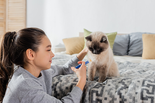 smiling girl making injection to cat with toy syringe in bedroom