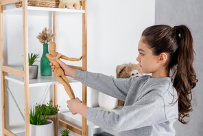 side view of girl playing with toy human figurine near rack with potted plants