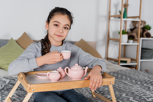 positive girl  while holding cup near toy tea set