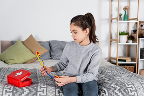 girl sitting on bed near first aid kit and holding toy stethoscope