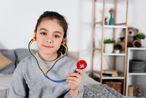 cheerful brunette girl with toy stethoscope smiling at camera