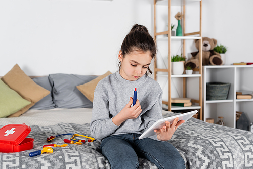 girl with toy syringe looking at digital tablet while playing in bedroom