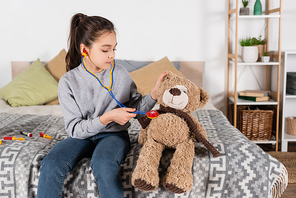 brunette preteen girl playing at home and examining teddy bear with toy stethoscope