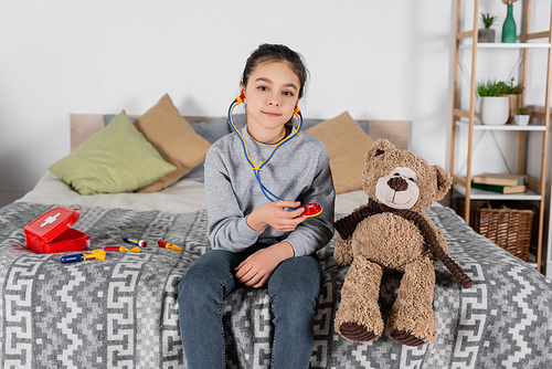 girl with toy stethoscope  near teddy bear and medical set