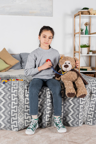 girl  while playing with teddy bear and toy stethoscope in bedroom