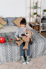 high angle view of girl examining teddy bear with neurological malleus while playing on bed