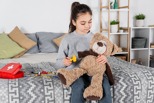 preteen girl examining teddy bear with toy neurological malleus in bedroom