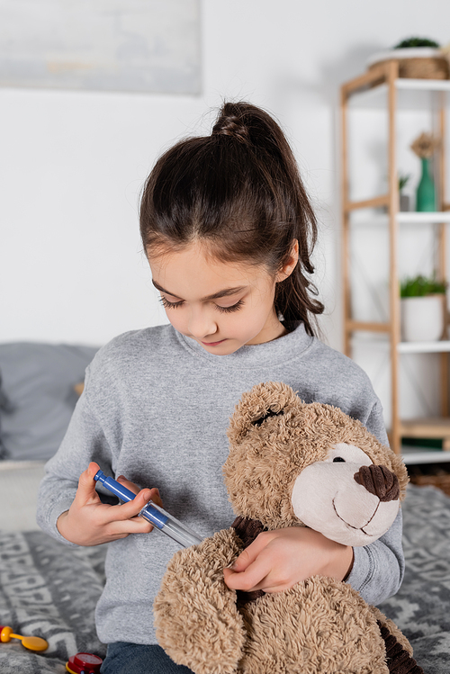 brunette preteen girl making injection to teddy bear with toy syringe
