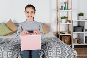 cheerful girl  while sitting on bed with pink box
