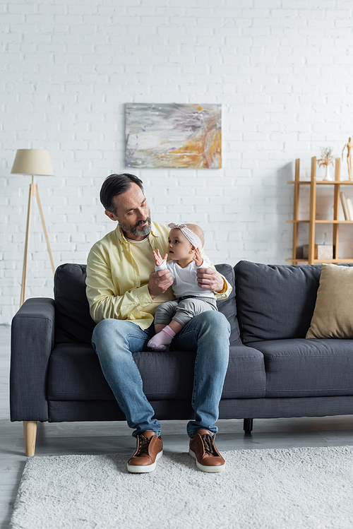 Mature man holding toddler kid on couch