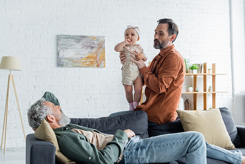 Mature homosexual man holding child near partner on couch