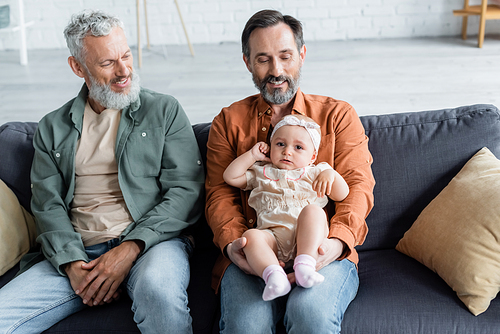 Smiling same sex couple with daughter sitting on couch