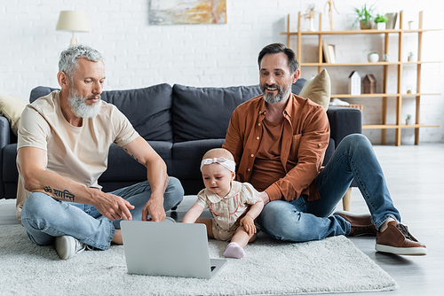 Smiling homosexual man sitting near daughter, laptop and partner