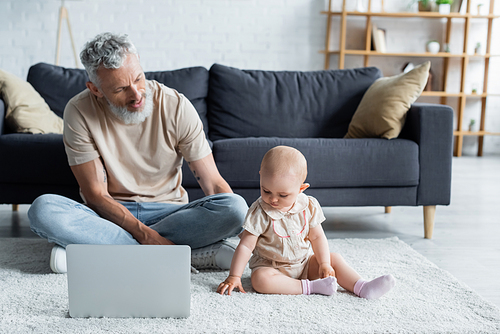 Toddler girl sitting on carpet near father with laptop
