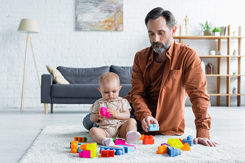 Father playing colorful building blocks with toddler daughter