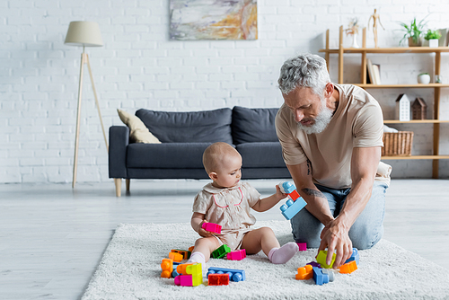 Mature father playing building blocks with child on carpet
