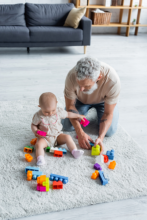 High angle view of toddler kid holding building blocks near father on carpet