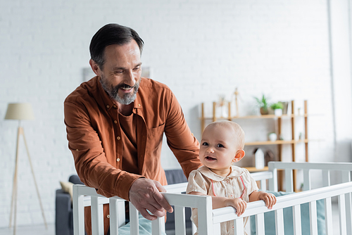Smiling mature father looking at baby daughter in crib