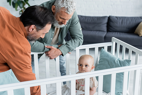 Baby girl sitting in crib near homosexual parents