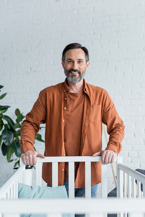 Smiling man standing near baby bed at home