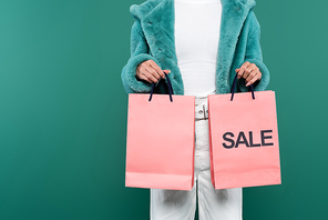 cropped view of woman in faux fur jacket holding sale shopping bags isolated on green