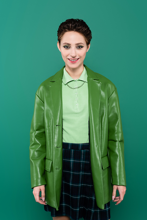 happy brunette woman in leather jacket and plaid skirt  isolated on green