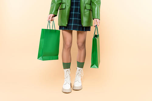 cropped view of woman in plaid skirt and white lace-up boots holding shopping bags on beige