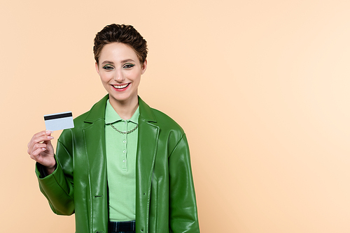 joyful brunette woman with credit card  isolated on beige