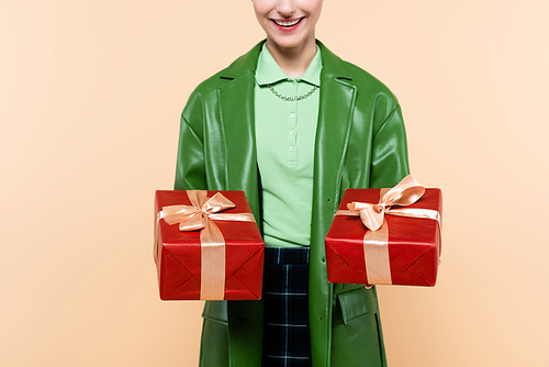cropped view of smiling woman in green jacket holding red gift boxes isolated on beige