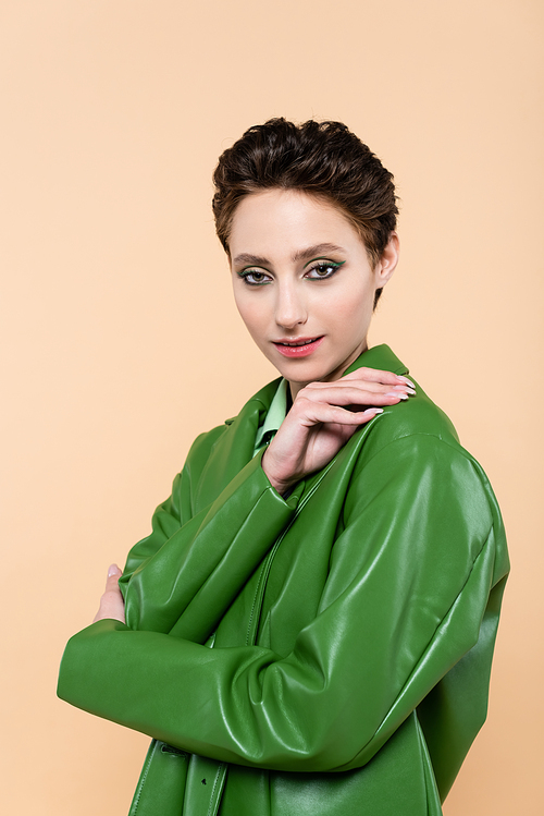 brunette woman with short hair, wearing green leather jacket, posing isolated on beige