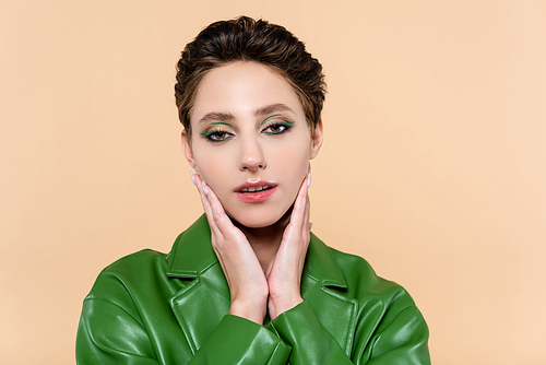 brunette woman in green leather jacket touching face while  isolated on beige