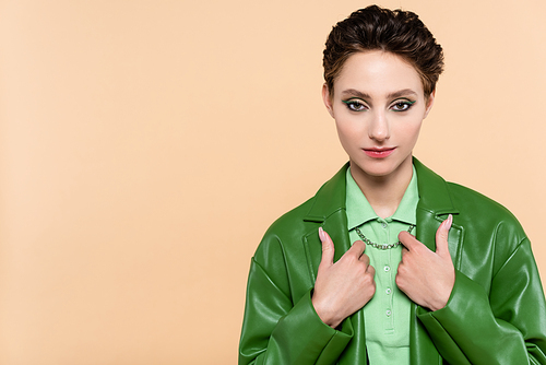 young woman in green leather jacket  while posing isolated on beige