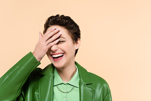 young excited woman covering face with hand while laughing isolated on beige
